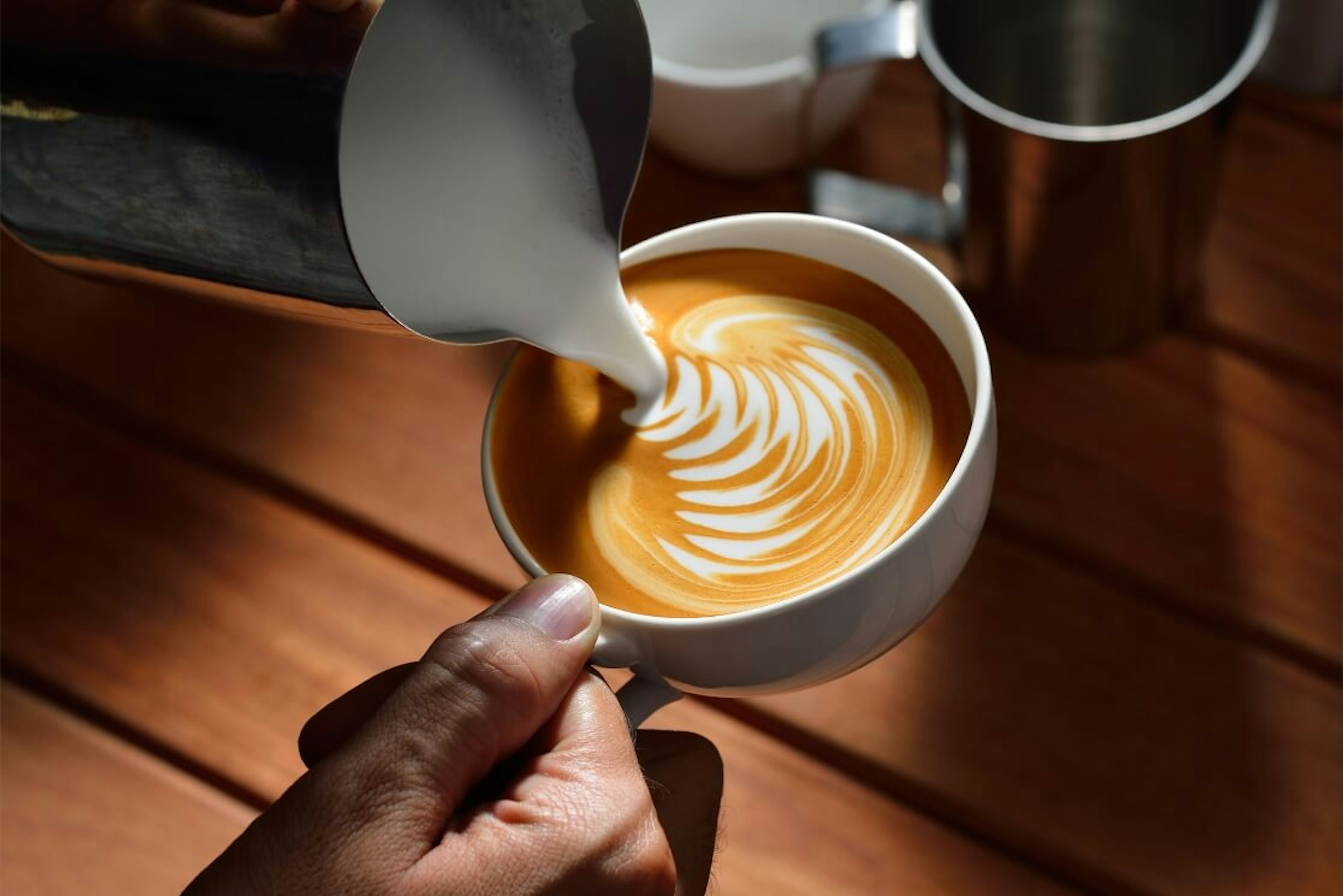 Una persona aprende a cremar y espumar la leche para hacer arte latte como un profesional mientras aprendes a abrir una cafetería desde cero.
